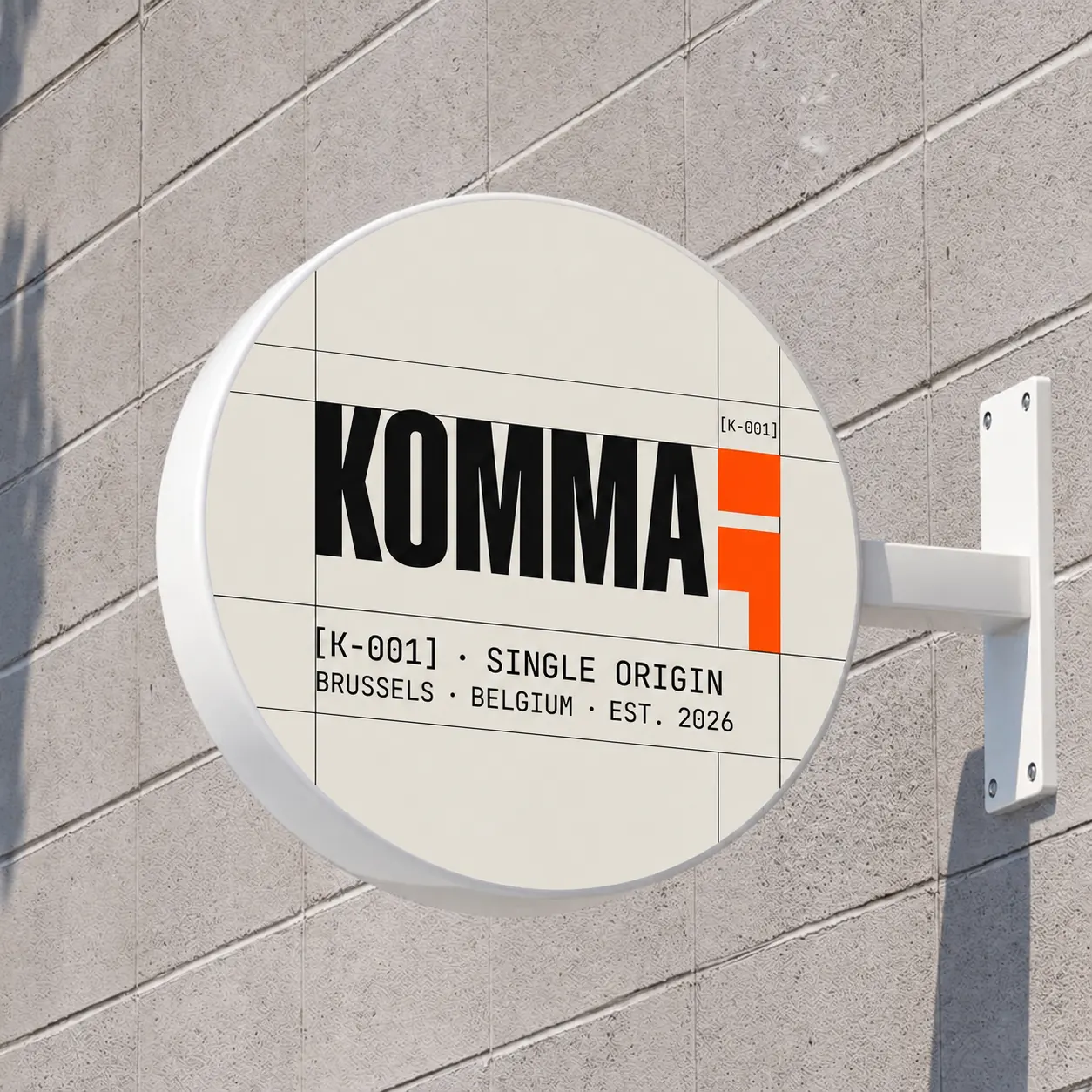 Signalétique murale ronde KOMMA fixée sur un mur de pierre, indiquant SINGLE ORIGIN · BRUSSELS · BELGIUM · EST. 2026.