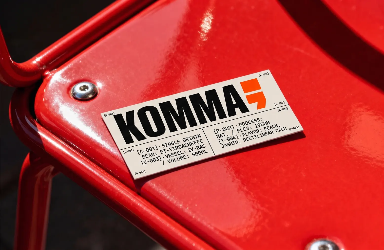 Sticker KOMMA collé sur une chaise rouge métallique, avec spécifications C-001, V-003, P-002, T-004.
